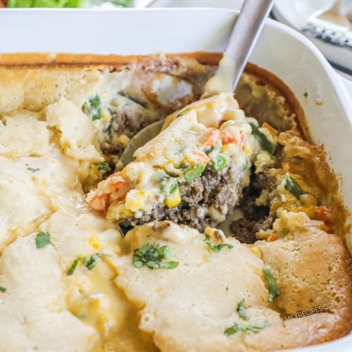 Serving spoon digging into ground beef cobbler in casserole dish