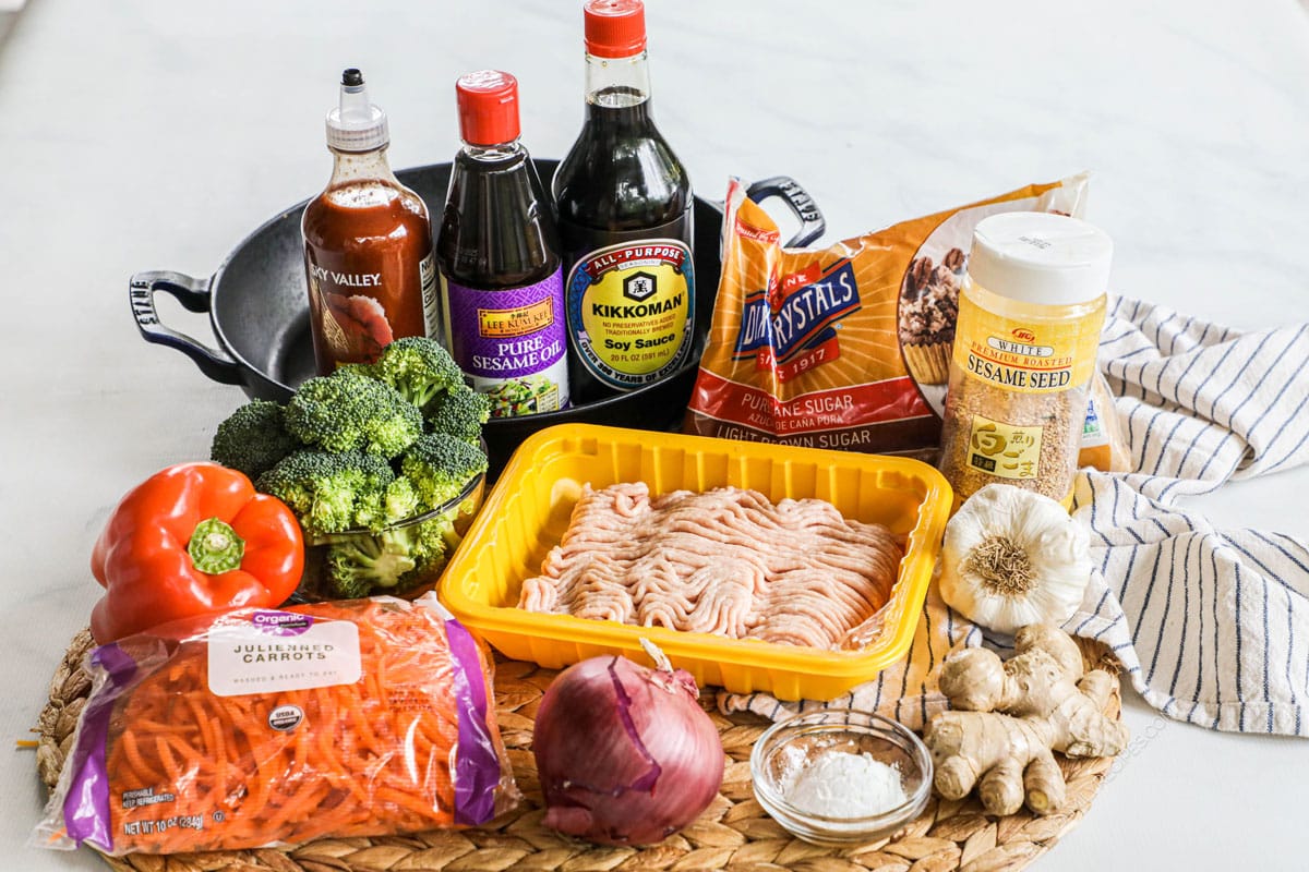 Ingredients to make ground chicken stir fry with soy sauce, garlic, and vegetables including peppers, broccoli, onion, and carrots.