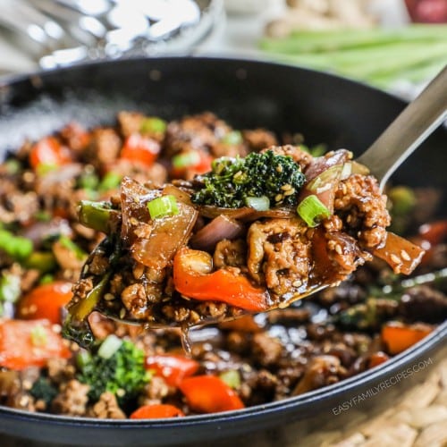 A spoon scooping ground chicken vegetable stir fry from a pan.