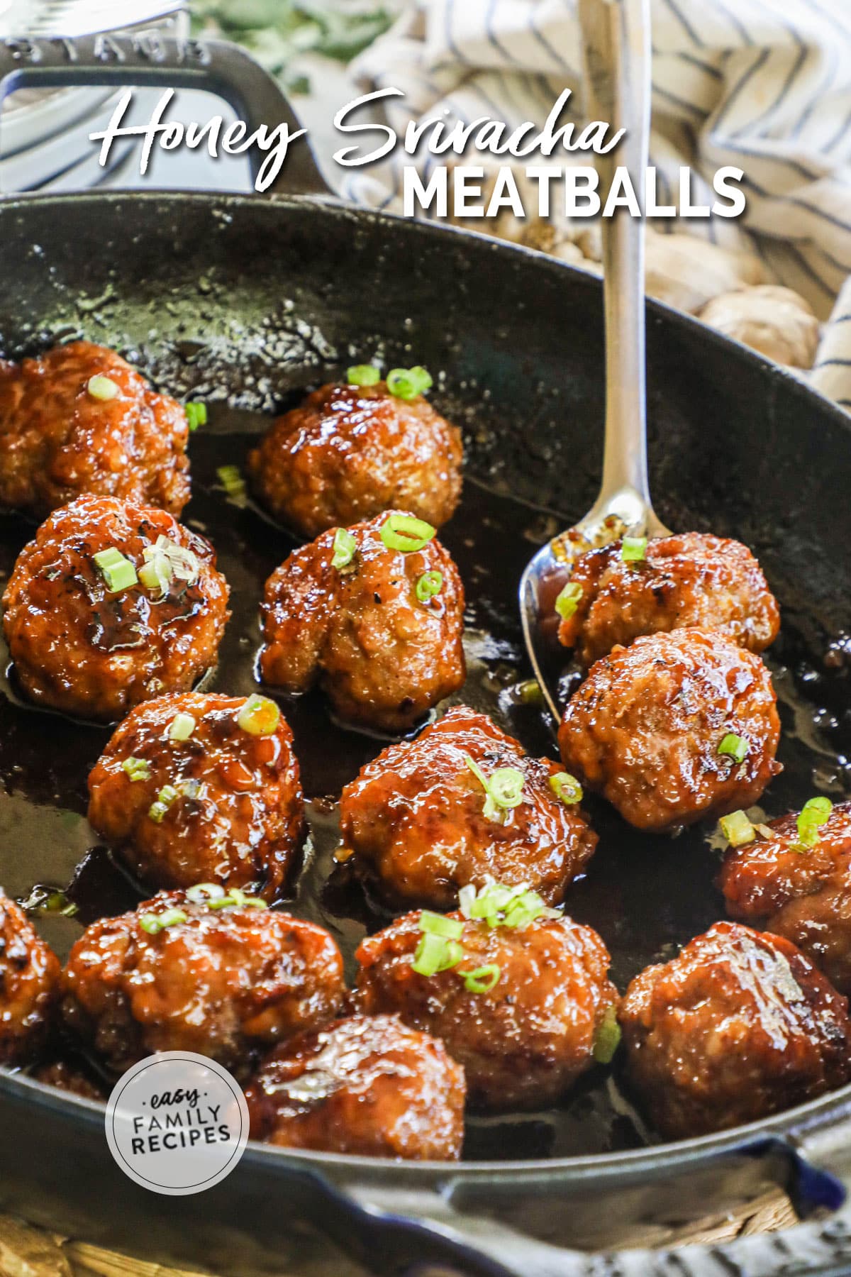 Spoon lifting two honey sriracha meatballs from cast iron skillet