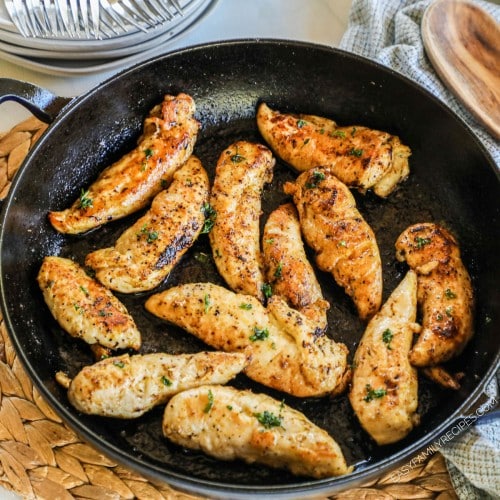 a pan of lemon pepper seasoned chicken tenders cooked and sprinkled with parsley.