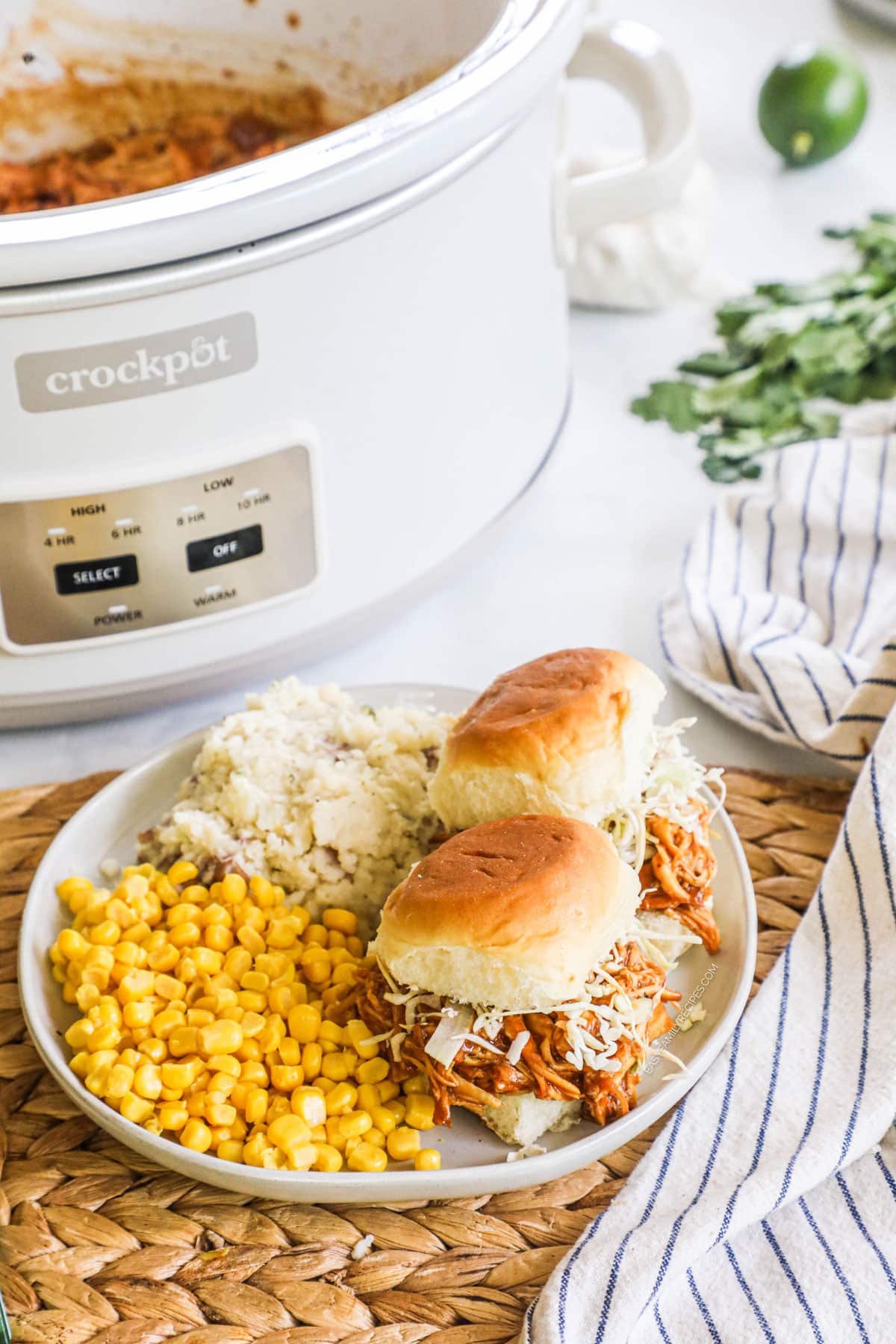 overhead of a plate filled with bbq chicken ranch sliders, corn, and mashed potatoes next to a crockpot.