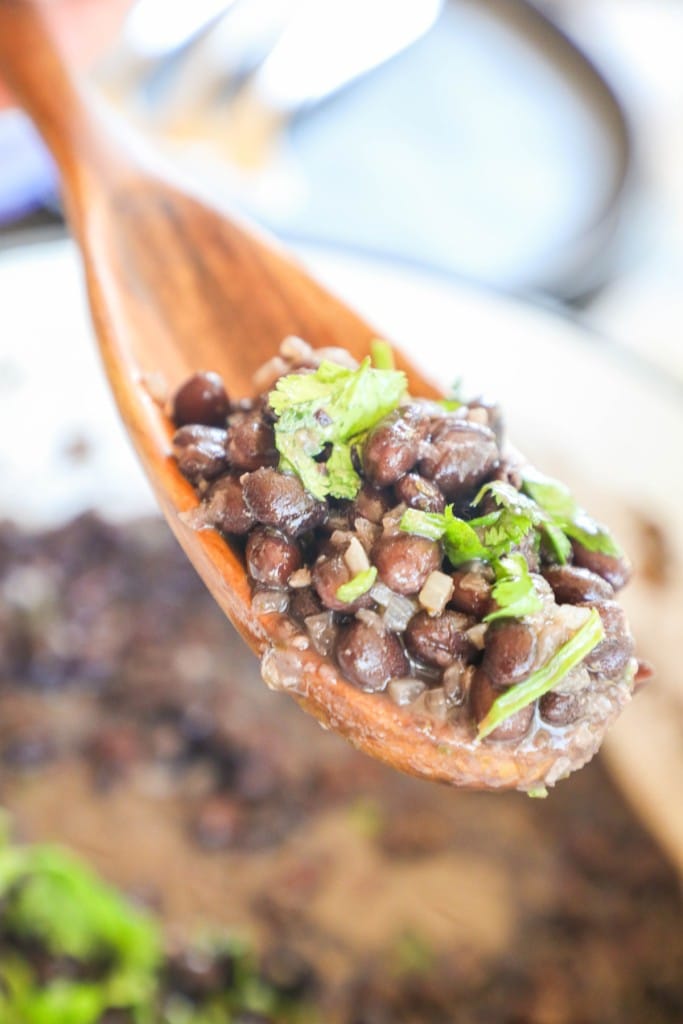 Scooping up a spoonful of black beans with a spoon to serve as a side dish