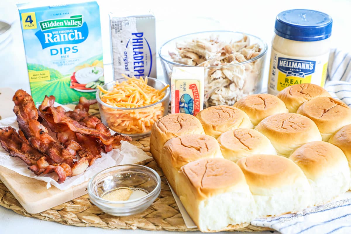 Ingredients for chicken bacon ranch sliders, including Hawaiian rolls, ranch seasoning, bacon, cheese, butter, mayo, chicken, cream cheese, garlic butter, and salt