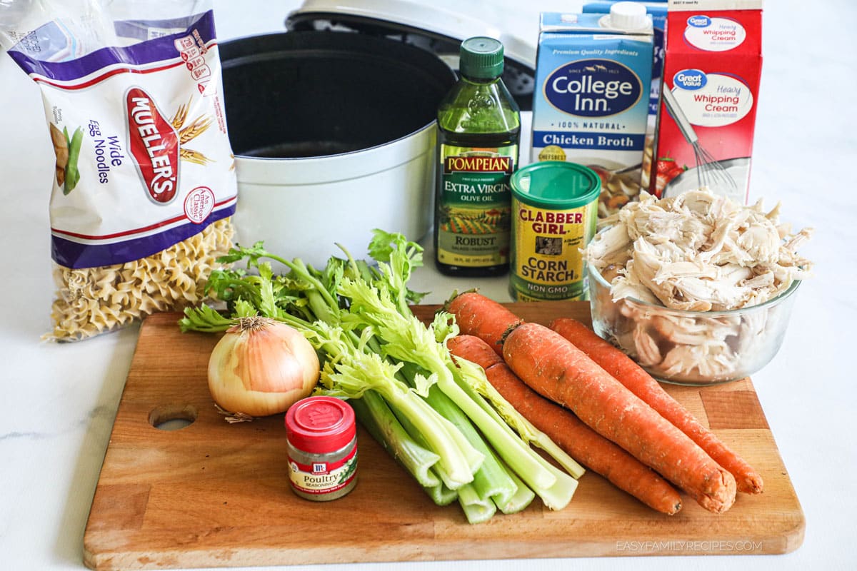 Ingredients for making creamy chicken noodle soup including rotisserie chicken, carrots, celery, onion, broth, and cream.