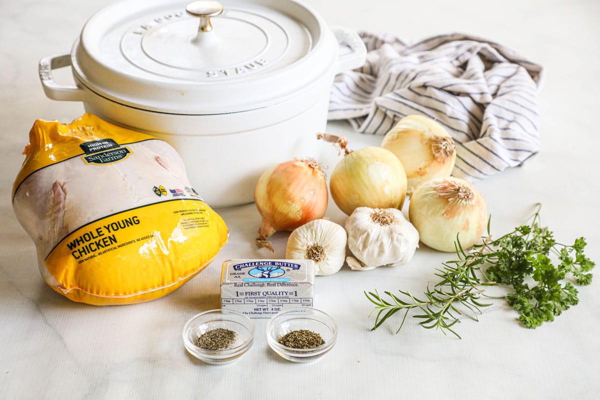 Ingredients for Dutch oven roast chicken, including whole chicken, butter, herbs, garlic, and onions