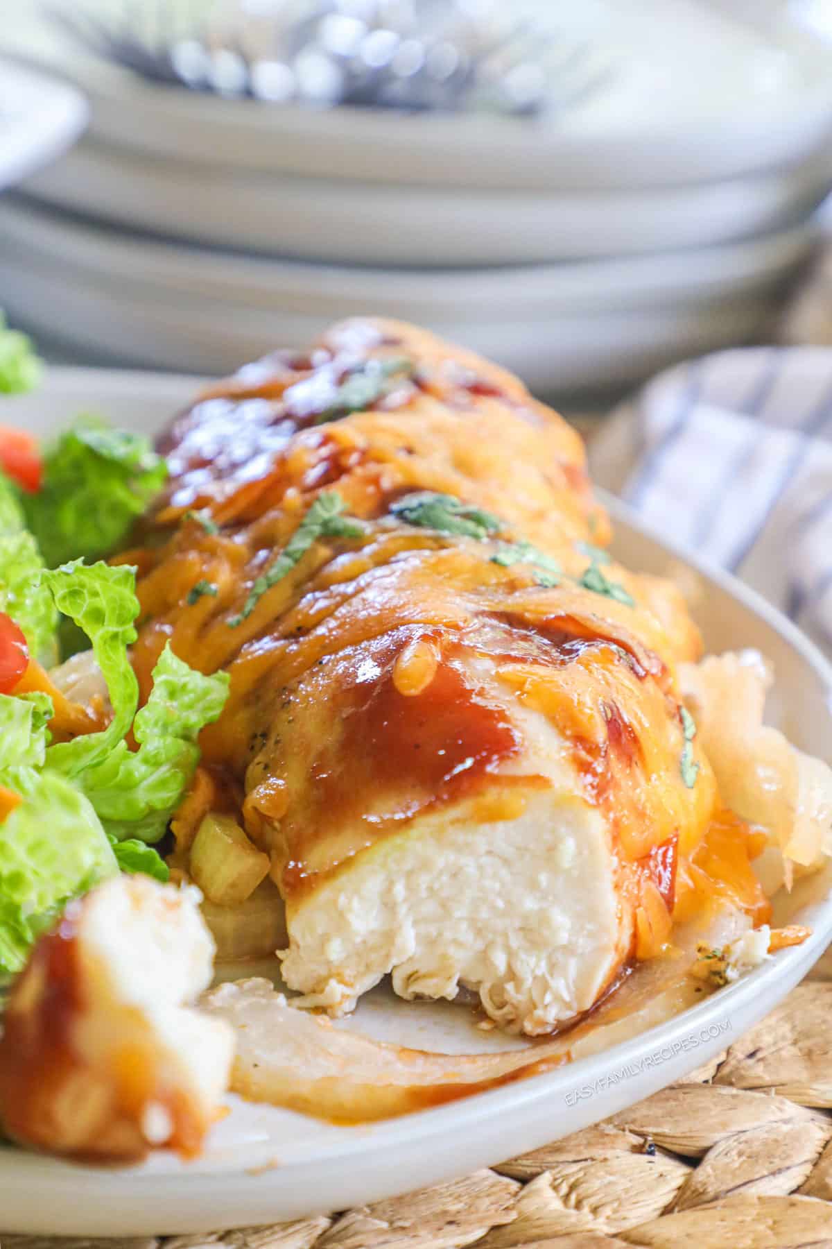 A plate with a baked BBQ chicken breast topped with melted cheese and sliced open.