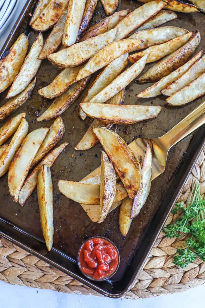 Potato wedges french fries on a baking sheet ready to serve with chicken wings