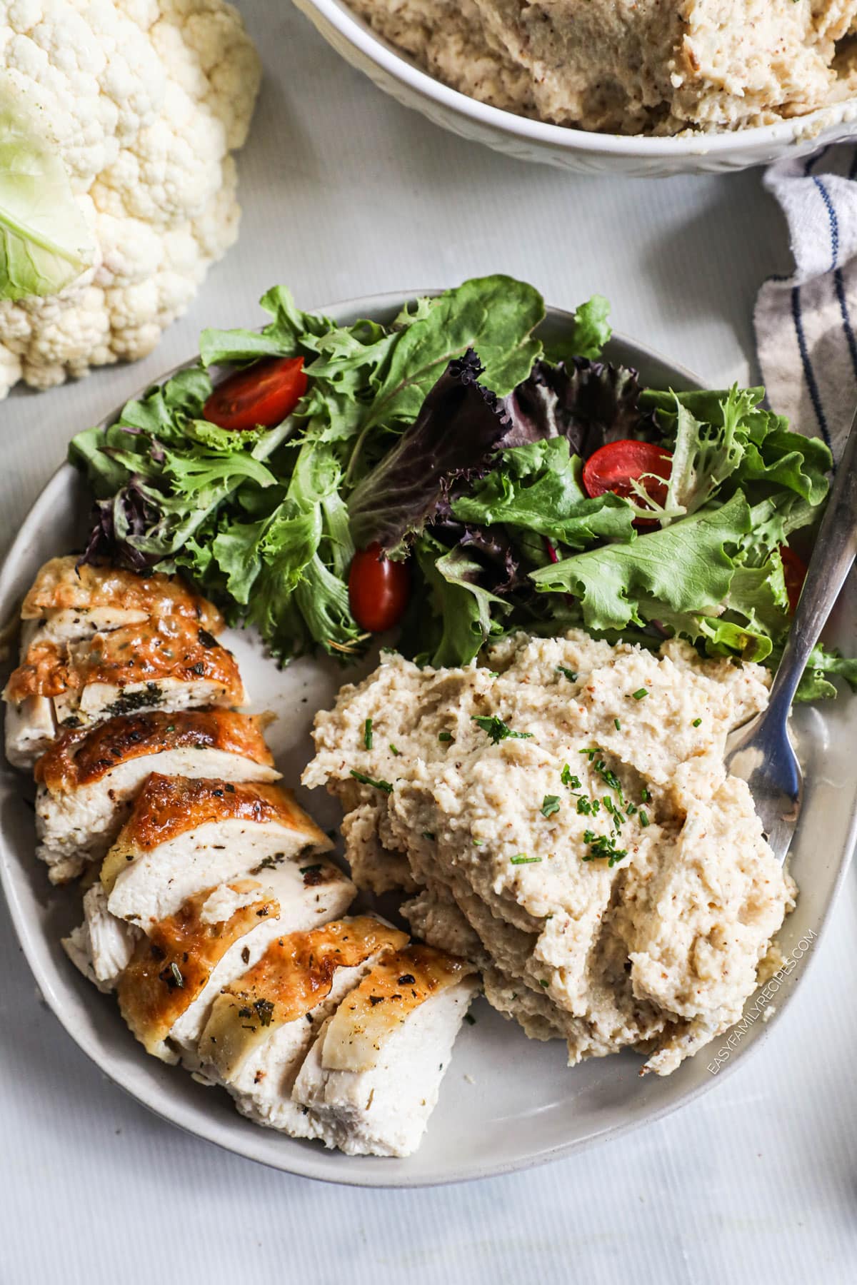 overhead of a plate with sliced chicken, cauliflower mash, and a side salad.