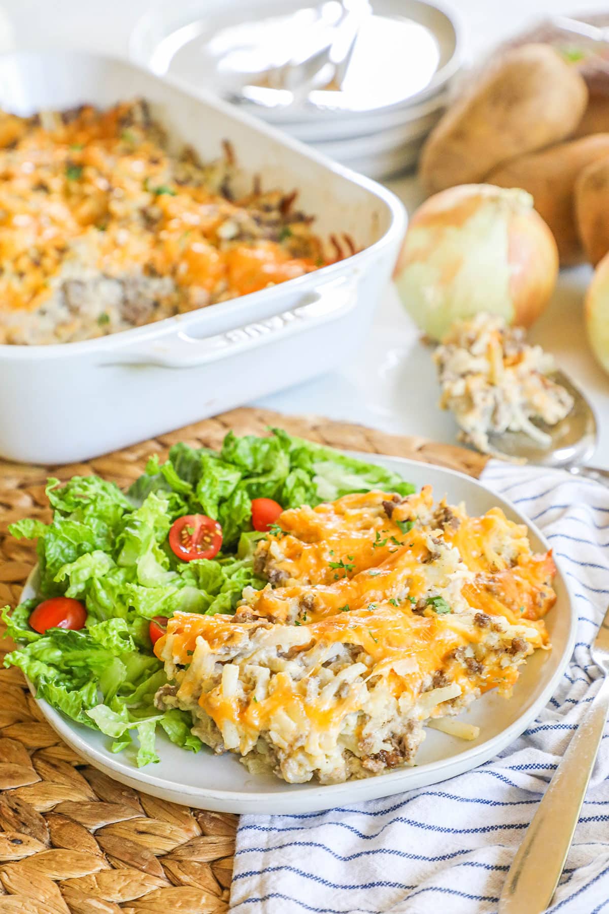 Ground beef hashbrown casserole served on a white plate with a green salad