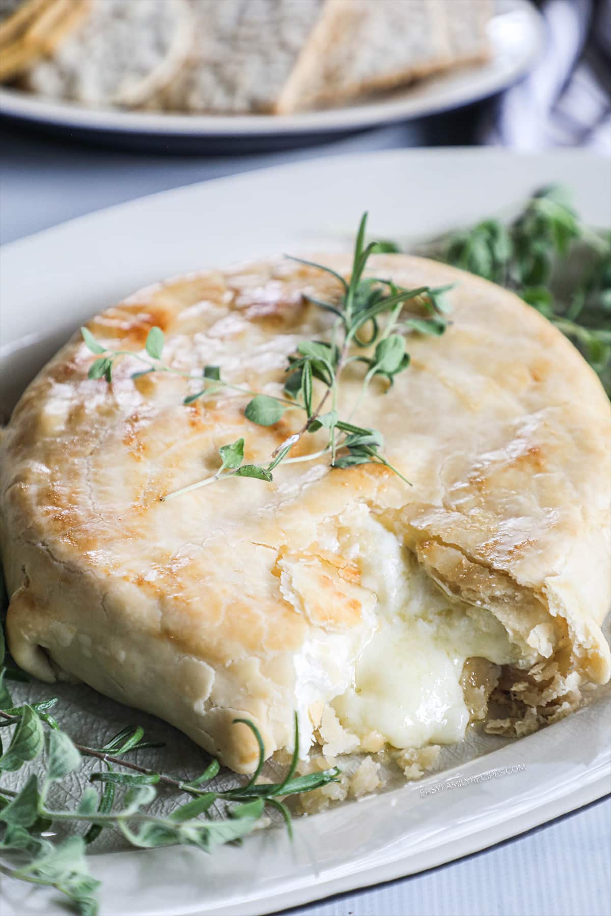 overhead of a wheel of baked brie in a golden pie crust topped with fresh herbs.