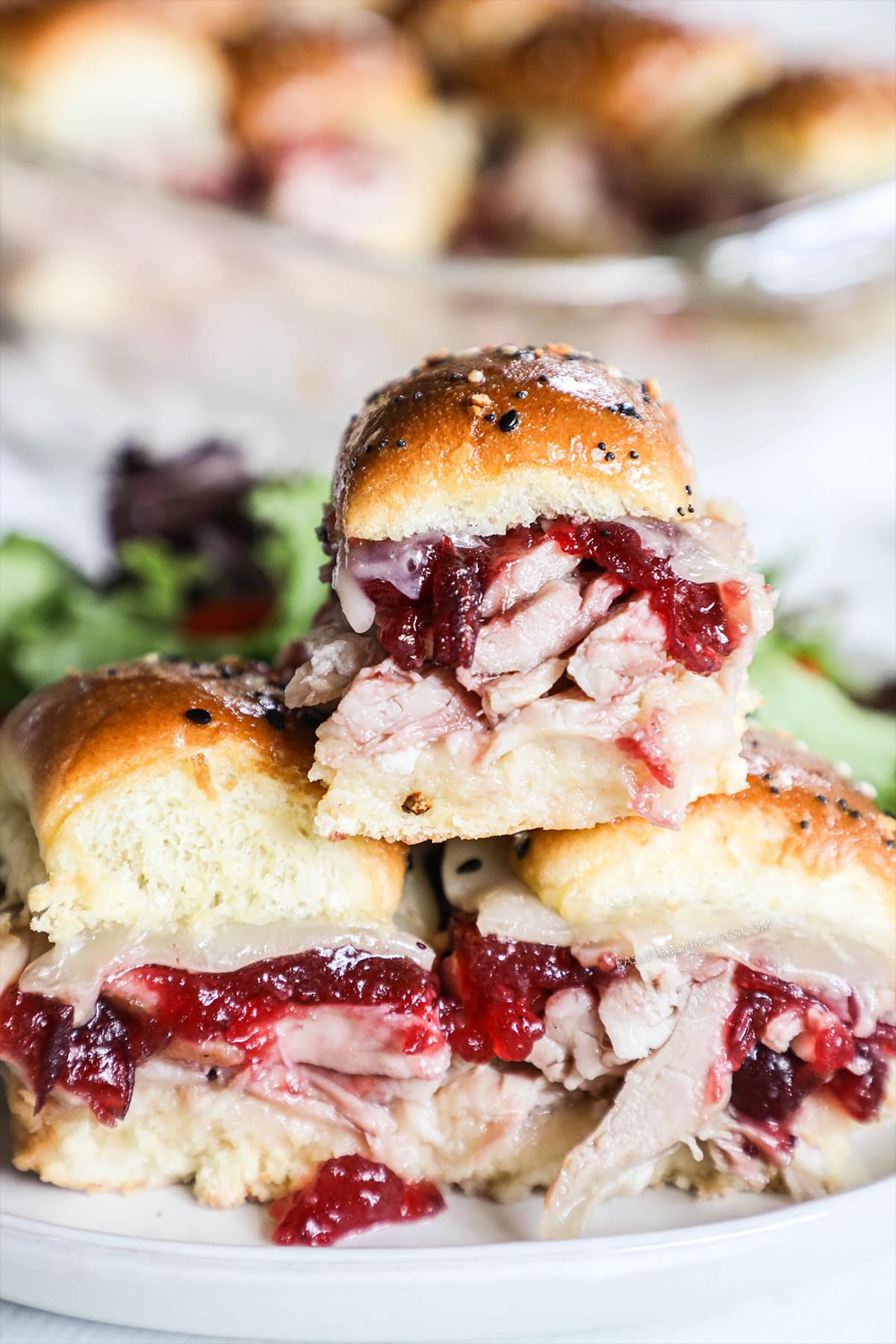 A stack of three turkey sliders with cranberry sauce on a white plate with green salad.