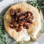 overhead of a wheel of baked brie in a golden pie crust topped with fresh herbs and pecans.