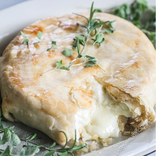 overhead of a wheel of baked brie in a golden pie crust topped with fresh herbs.