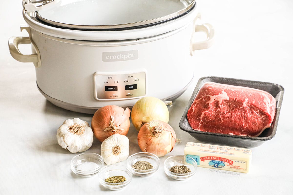 Ingredients for crockpot roast beef, including garlic, onions, beef, butter, and seasonings