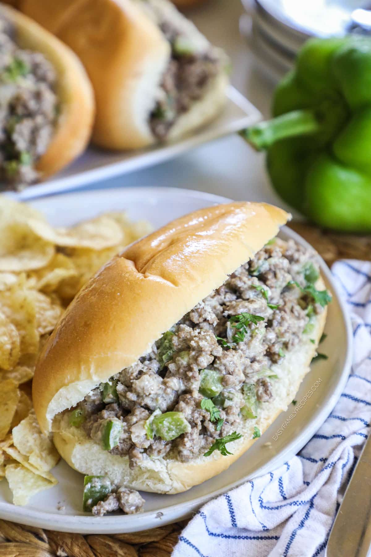 A ground beef philly cheesesteak sandwich on a plate with potato chips.
