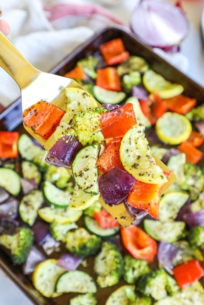 Roasted vegetables on a pan with a gold spoon scooping them up