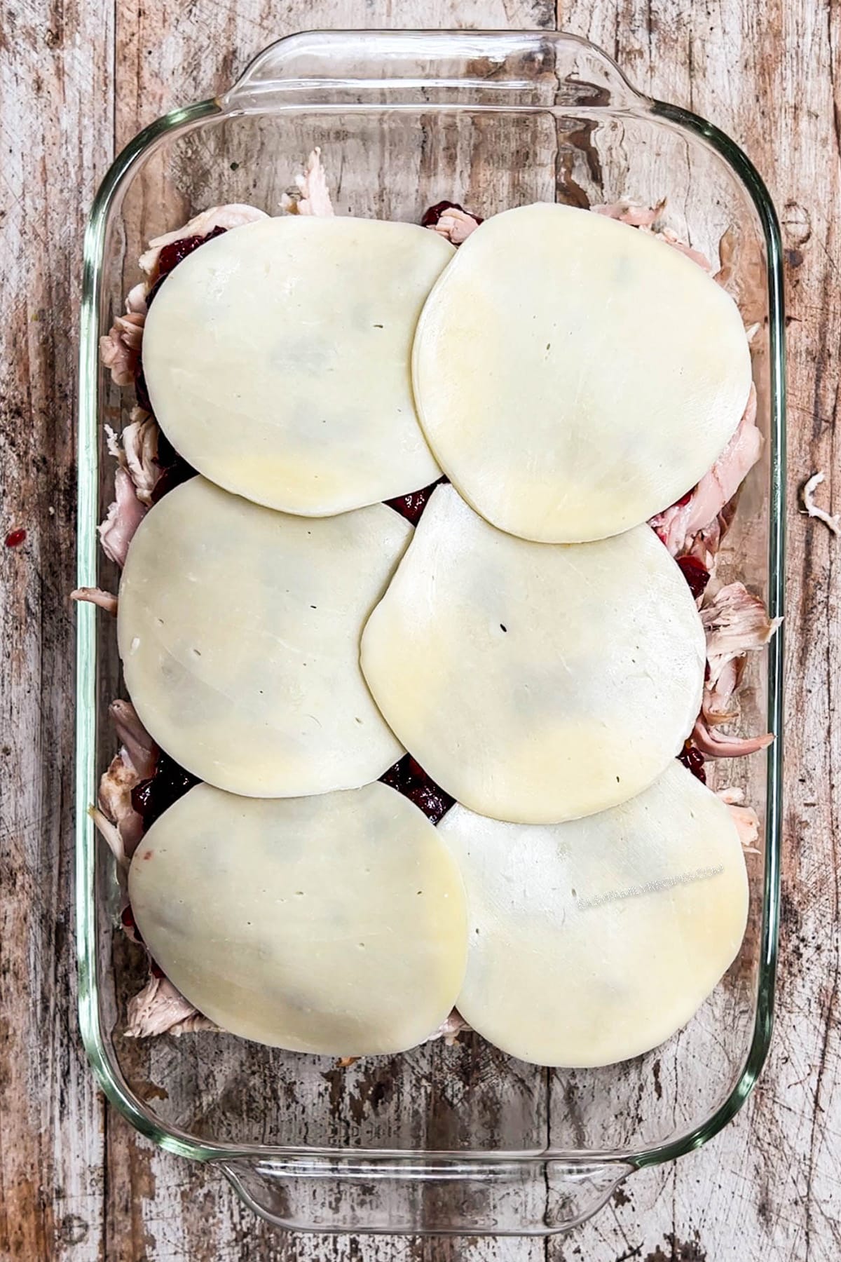 pan of shredded turkey topped with cranberry sauce and provolone cheese