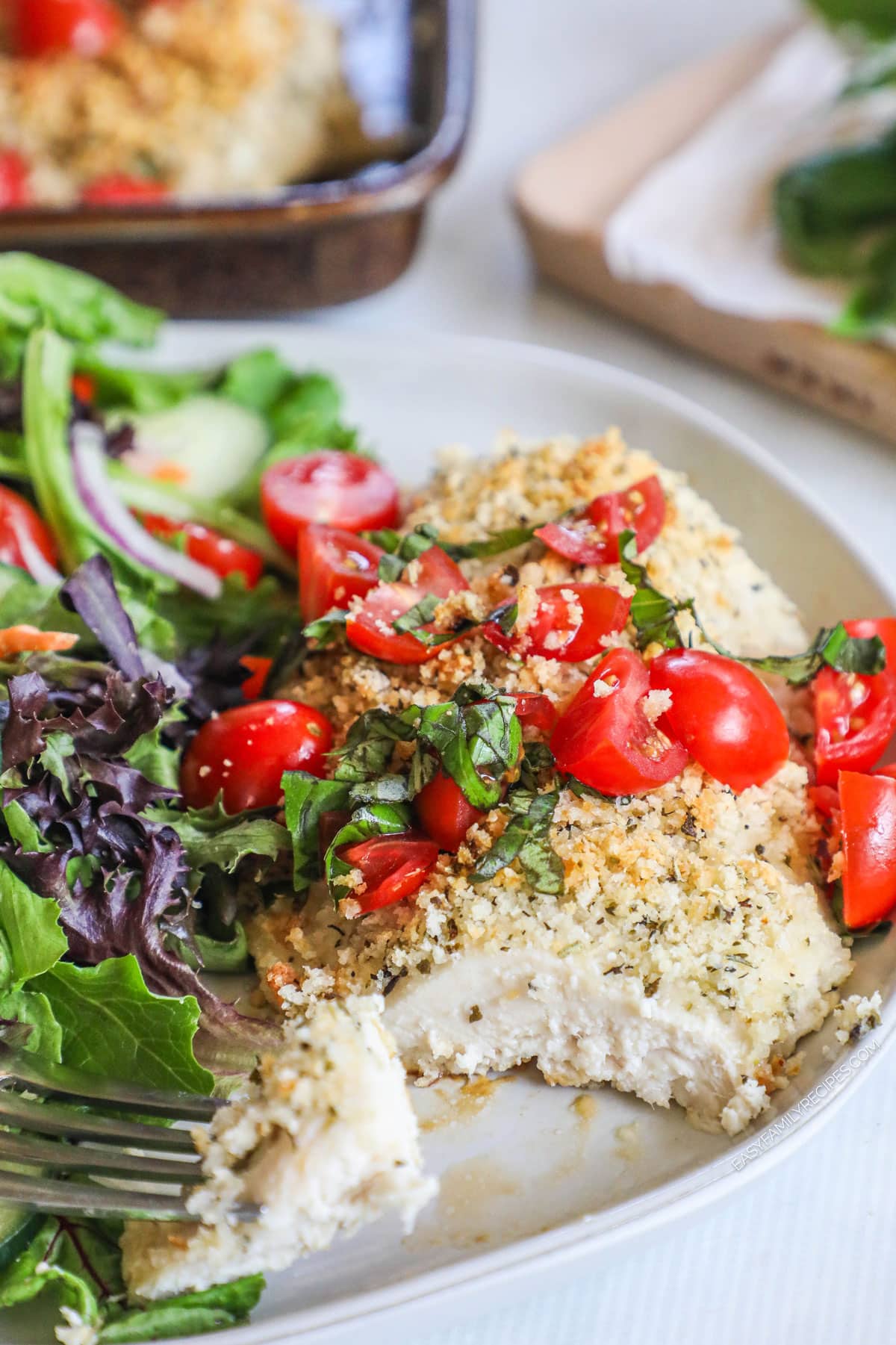 Juicy baked Italian chicken on plate with basil, tomatoes, and breadcrumbs