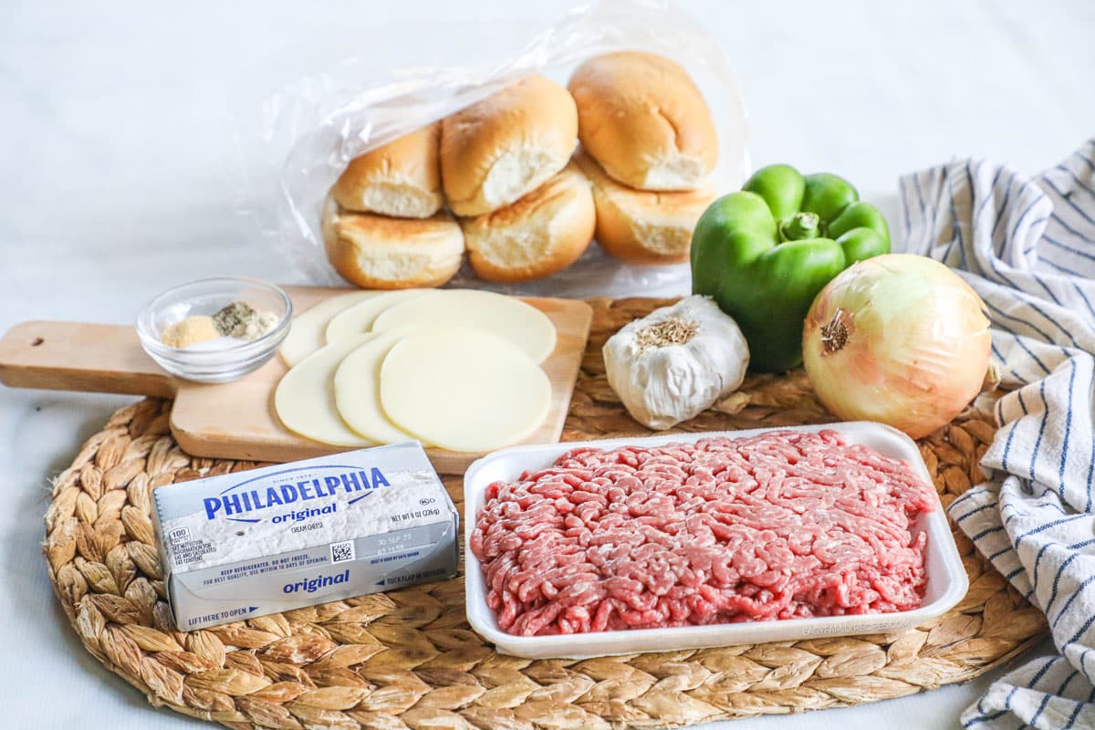 Ingredients for making easy philly cheesesteak sandwiches including ground beef, green bell pepper, an onion, buns, cheese, and seasonings.