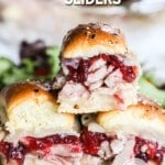 A stack of three turkey sliders with cranberry sauce on a white plate with green salad.