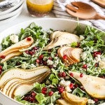 an arugula pear salad topped with sliced pear and pomegranate in a bowl.