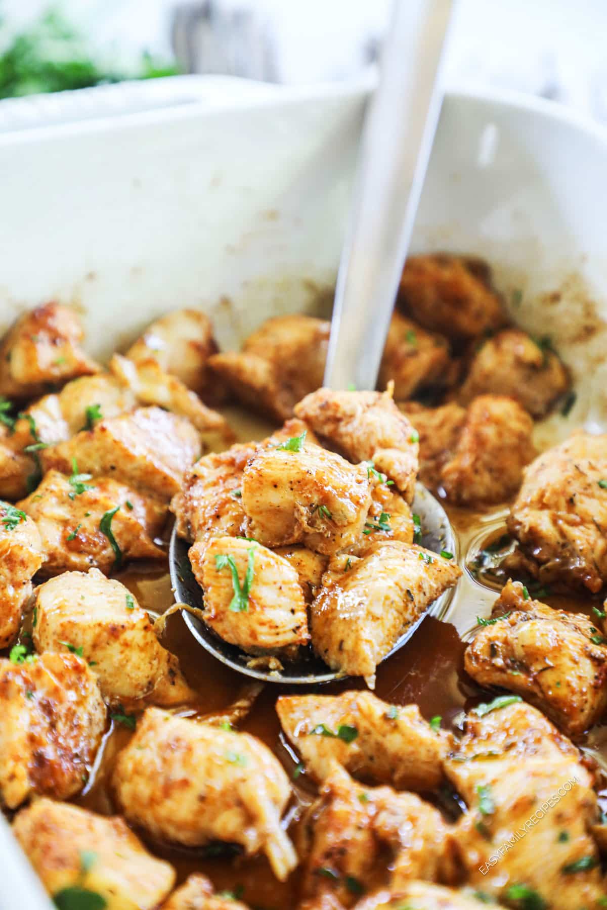 Spoon lifting chicken bites from baking dish