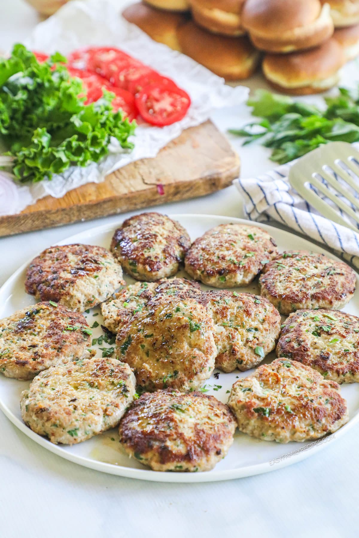 Plate of ground turkey patties with burger toppings in background