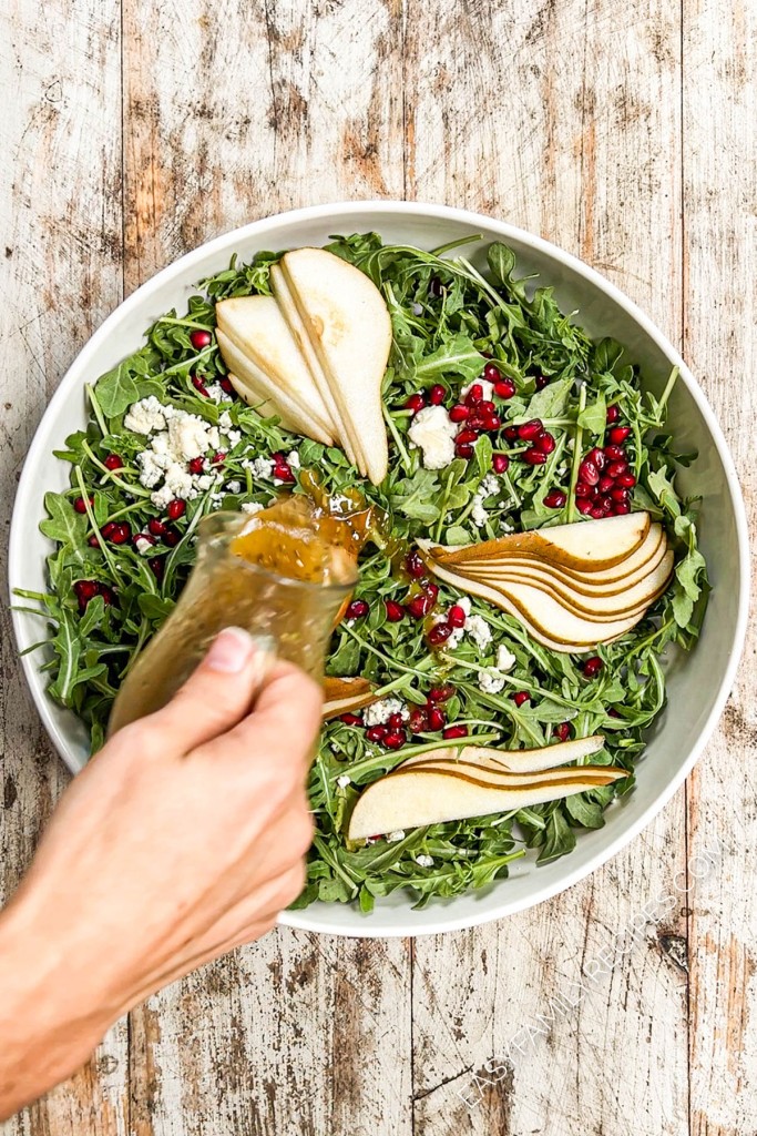 an arugula salad with pears being drizzled with red wine vinaigrette.