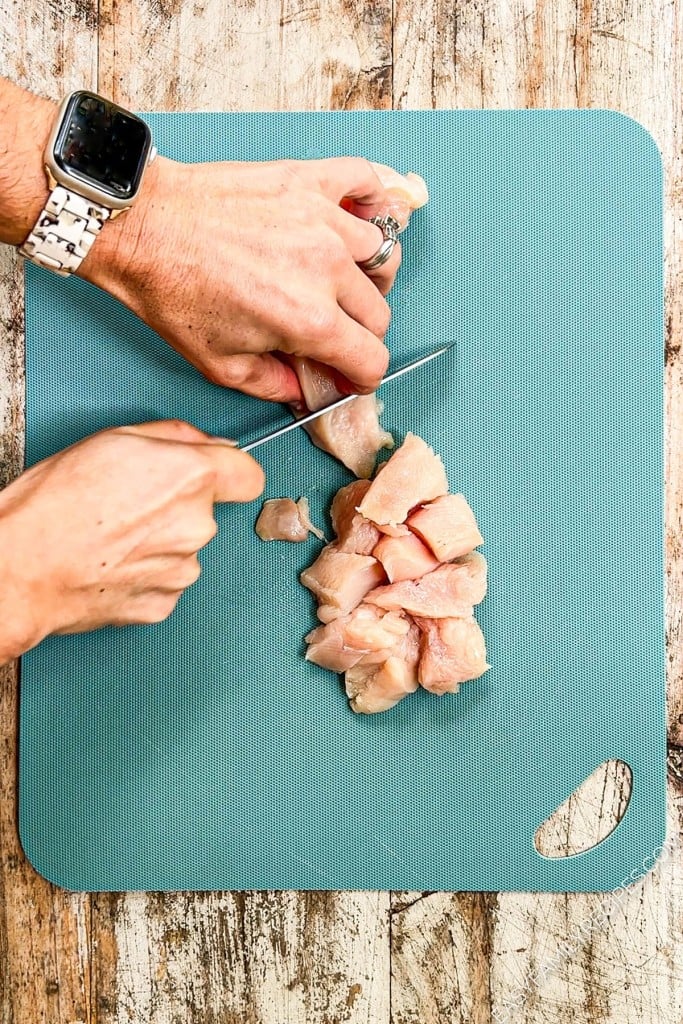 Overhead view of knife cutting chicken breast into bite-sized pieces