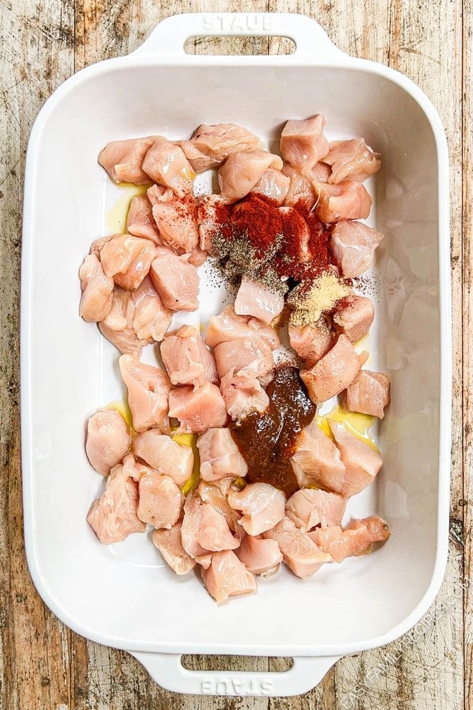Overhead view of chicken pieces in baking dish with seasonings and oil