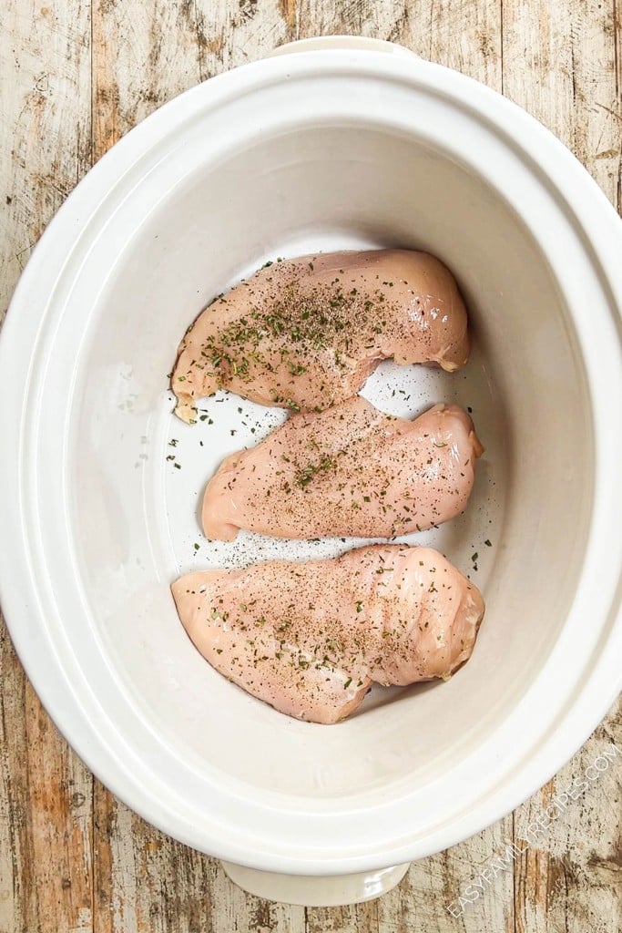 Chicken breast in a slow cooker with seasoning.