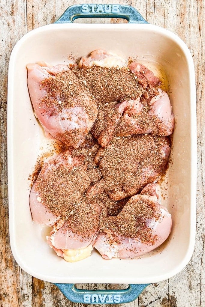 Seasoning added to chicken thighs in baking dish