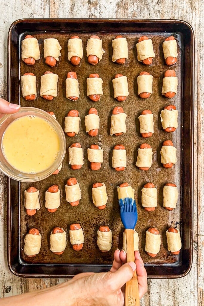 Brushing egg wash onto pigs in a blanket