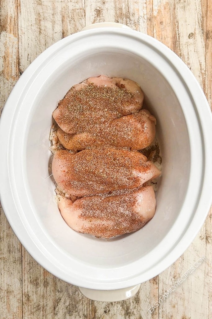 Overhead view of Southwest chili seasonings added to chicken breasts in crockpot