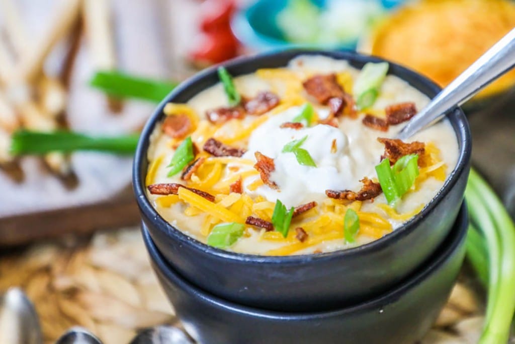 Baked potato soup in a black bowl with toppings