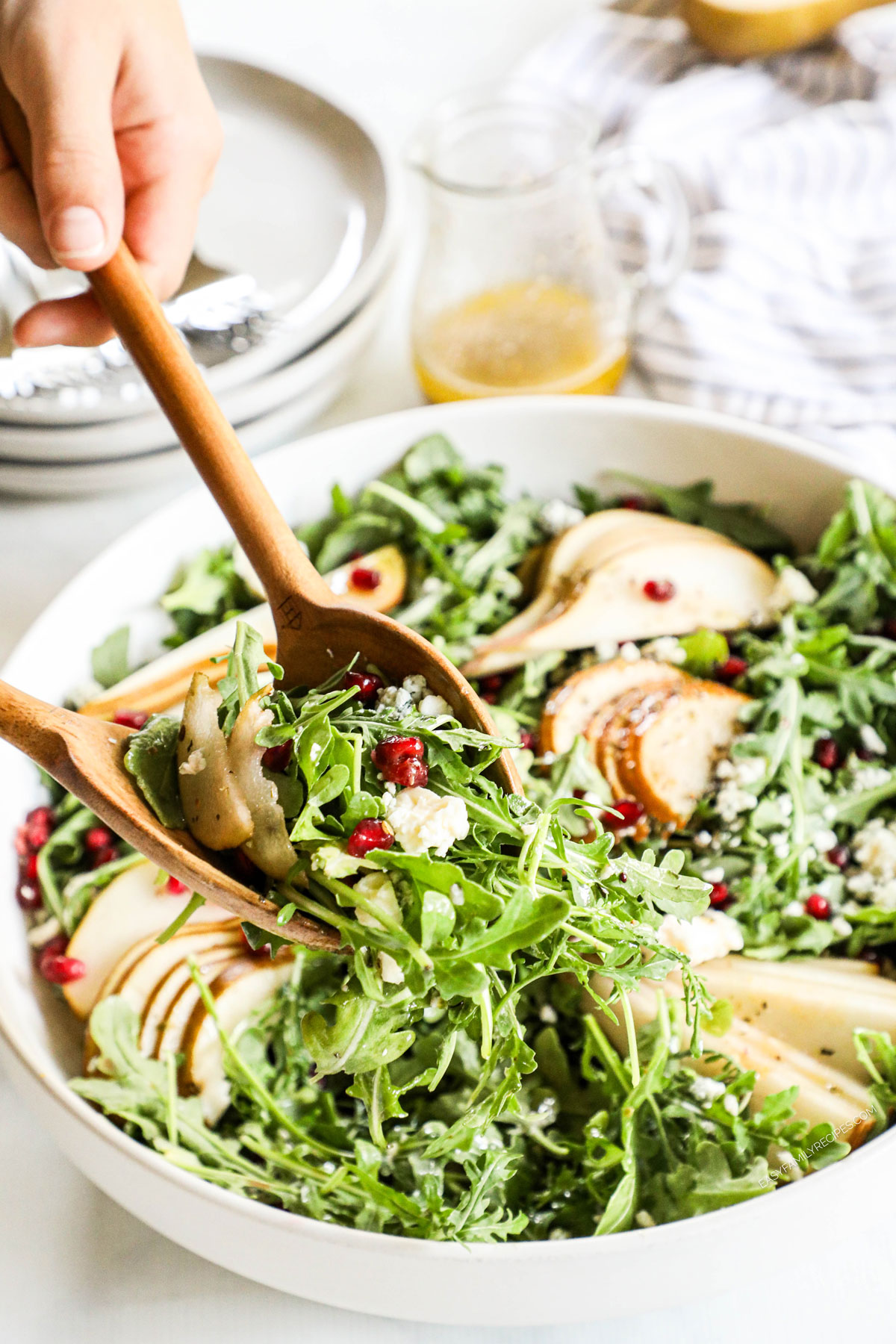 an arugula pear salad being tossed with wooden salad spoons.