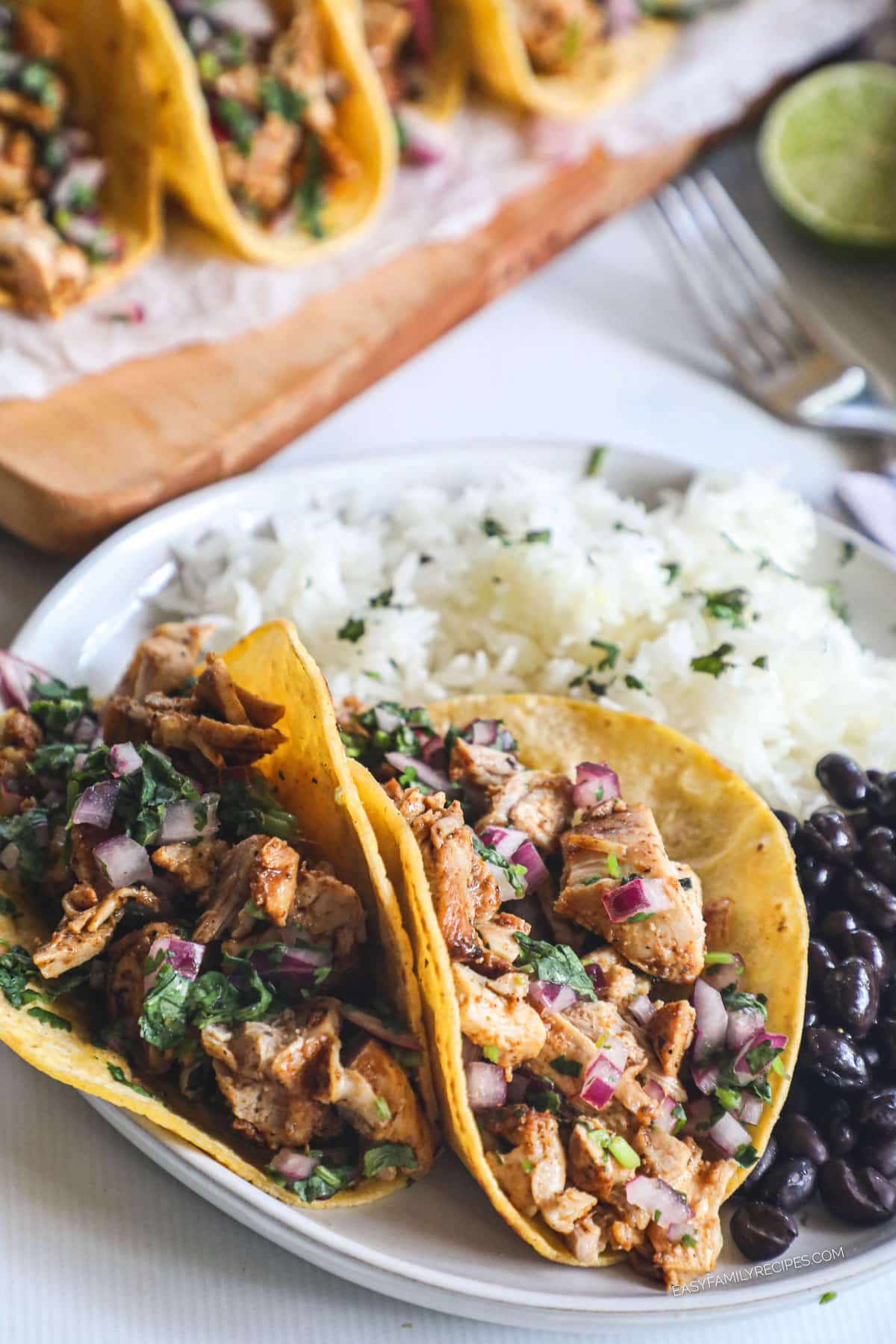Two Mexican street chicken tacos on plate with rice and beans