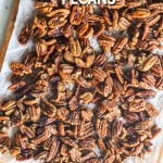 overhead image of sweet and spicy pecans spread out on a piece of parchment paper.