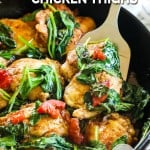 Tuscan chicken thighs in skillet with wilted spinach and tomatoes
