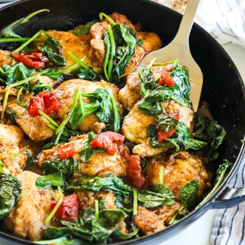 Spatula lifting Tuscan chicken thigh with spinach and tomatoes out of skillet