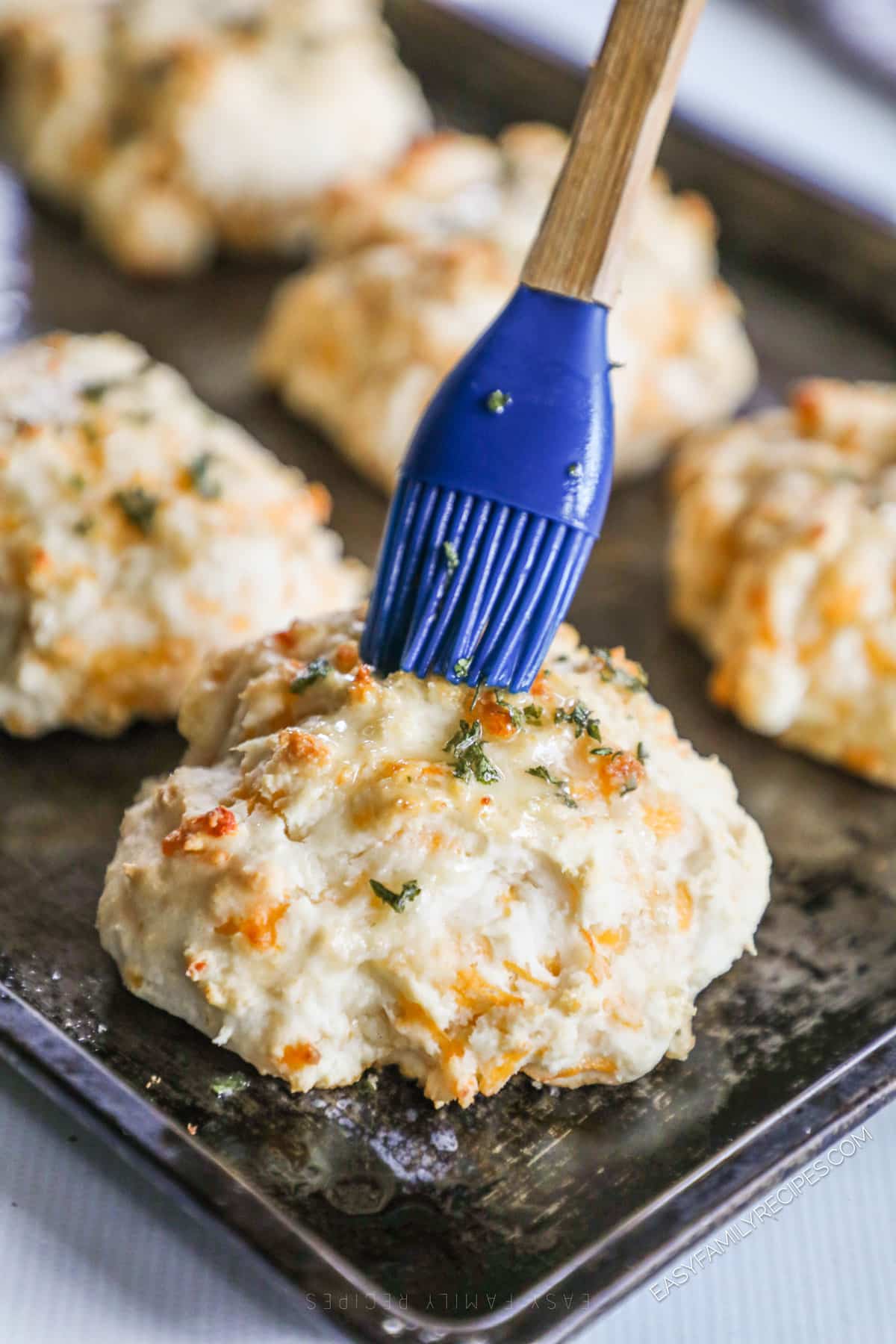 a closeup image of a cheddar bay biscuit being brushed with garlic butter.