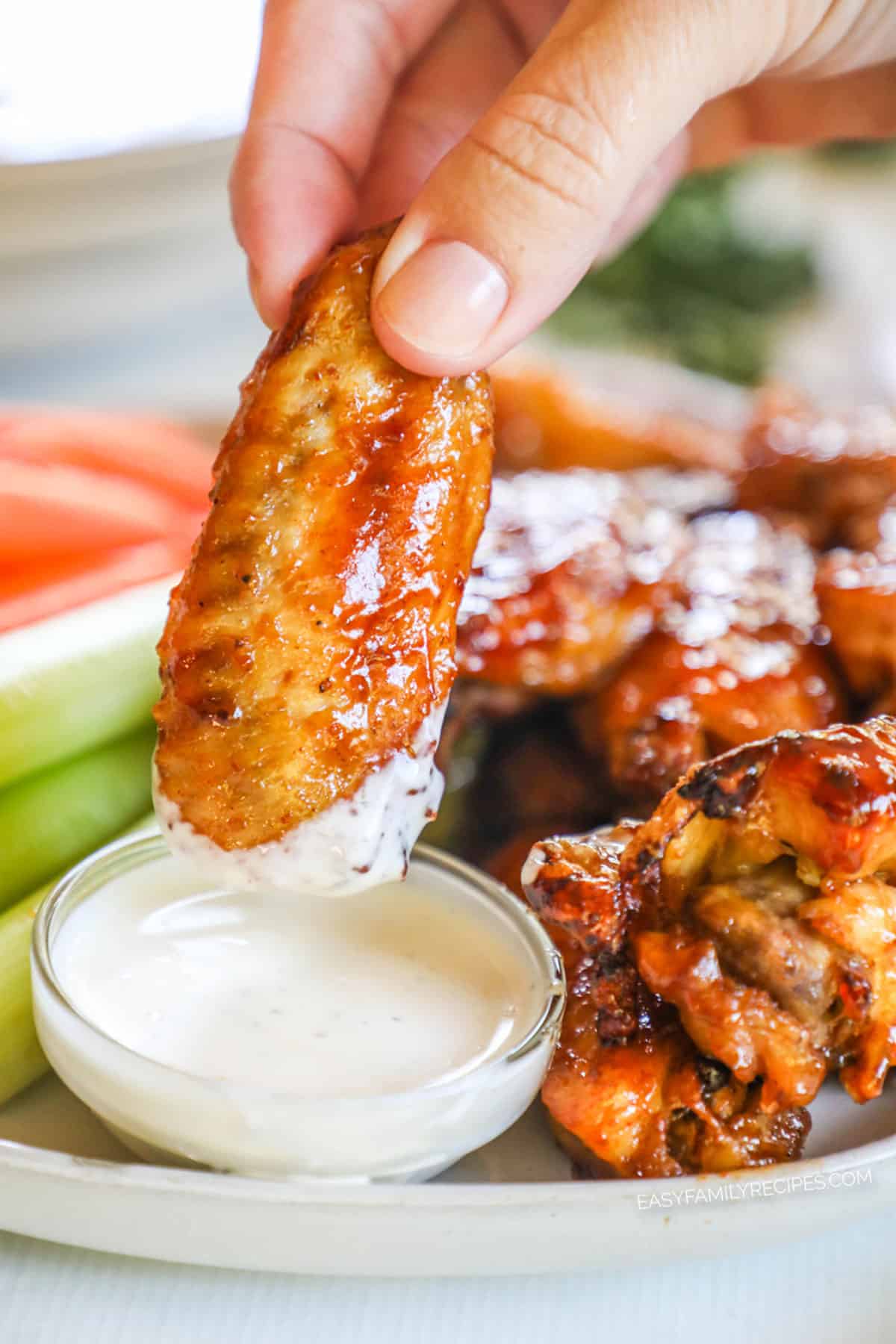 A person dips a honey BBQ chicken wing in creamy ranch dressing. 
