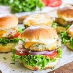 a platter of turkey burger sliders with melted cheese, lettuce, onion, and tomato.