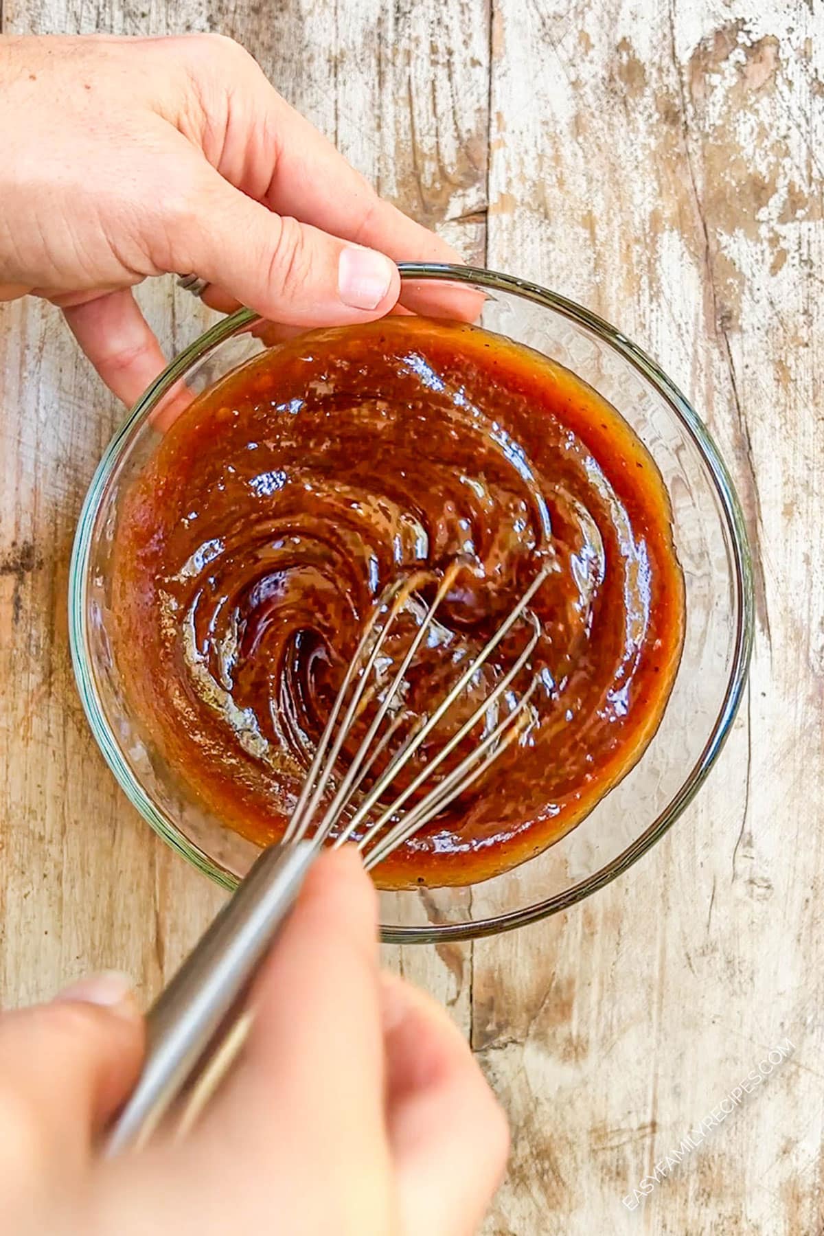 Honey and barbecue sauce are being whisked together in a glass bowl for honey BBQ sauce. 
