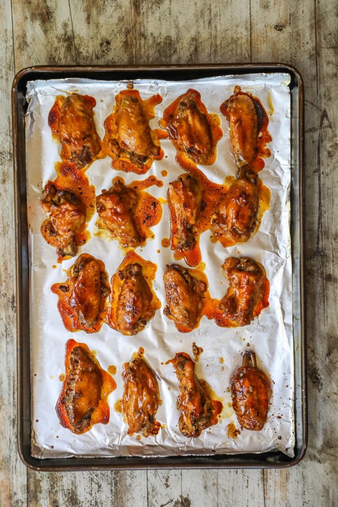Honey BBQ chicken wings have been removed from the oven and are sitting on a parchment-lined baking sheet. 