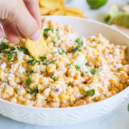 Mexican street corn dip in bowl with hand dipping some up with a chip.