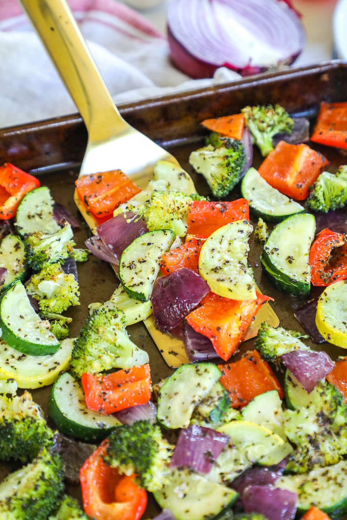 roasted vegetables in a pan being scooped by golden spatula