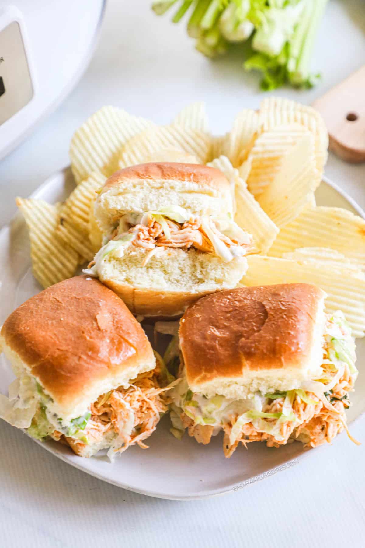 A platter of shredded buffalo chicken sliders on a plate with potato chips.