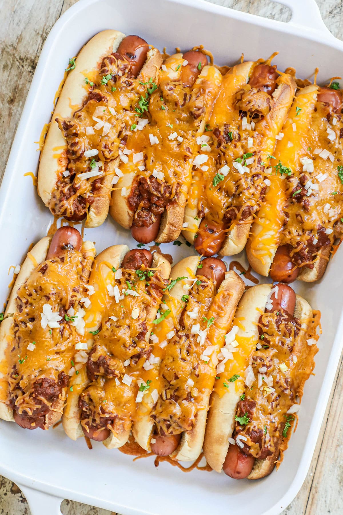 hot dogs topped with chili in a white casserole dish